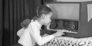 Niña junto a un antiguo receptor de radio representando el nacimiento de la radiodifusión.