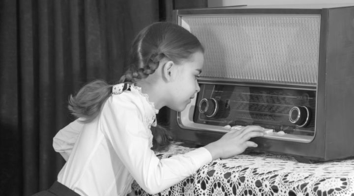 Niña junto a un antiguo receptor de radio representando el nacimiento de la radiodifusión.