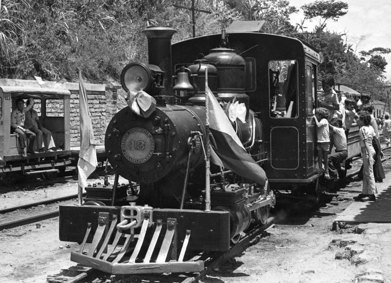 Locomotora histórica recorriendo una línea férrea entre montañas colombianas, símbolo del desarrollo ferroviario nacional.